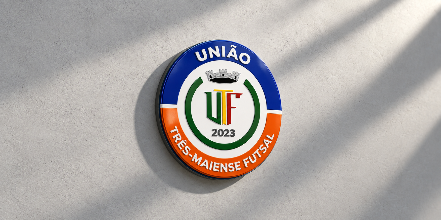 Escudo do União Três-Maiense Futsal em relevo sobre uma parede clara
